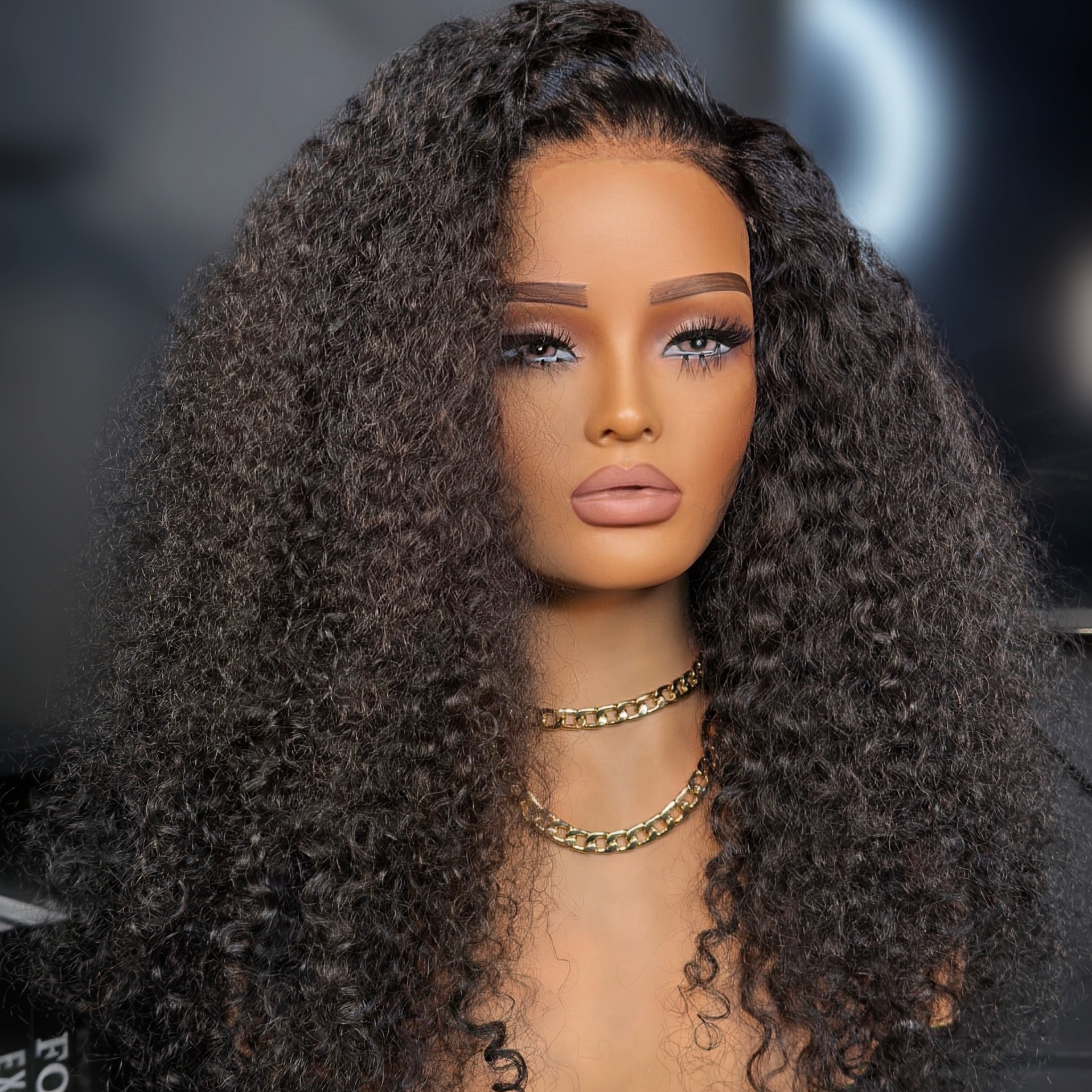 Mannequin head with long, curly black wig on a blurred background